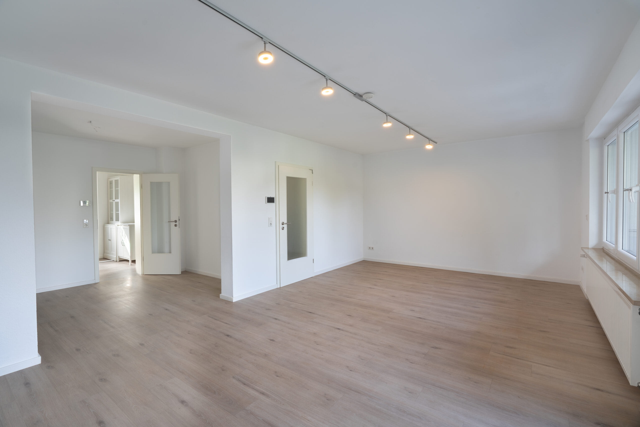 Leerer Wohnraum mit abgehängter Decke, Einbaustrahlern und Holzfußboden